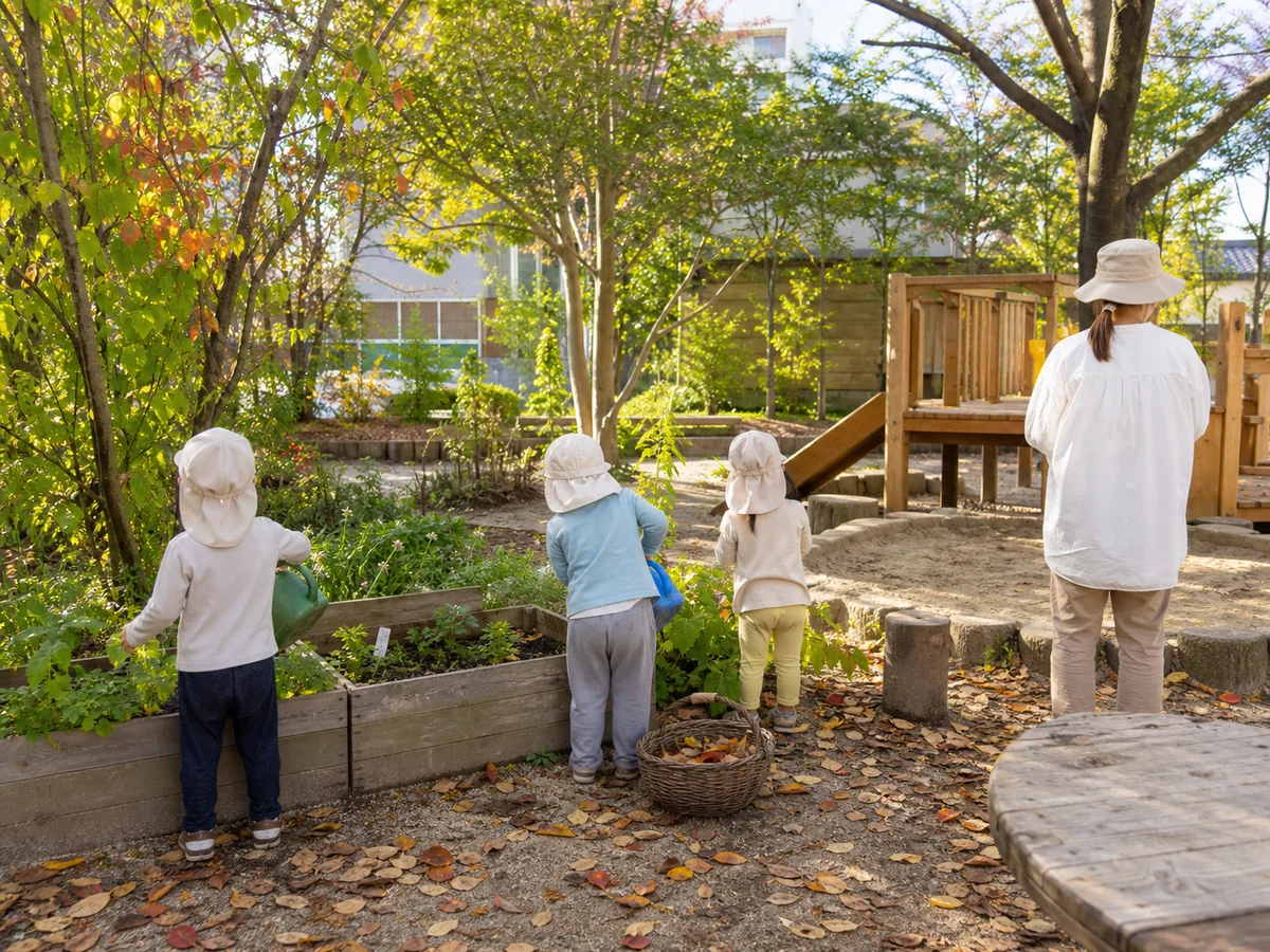 顔を写さず、園庭の菜園で水やりをする子どもたちと保育者の後ろ姿