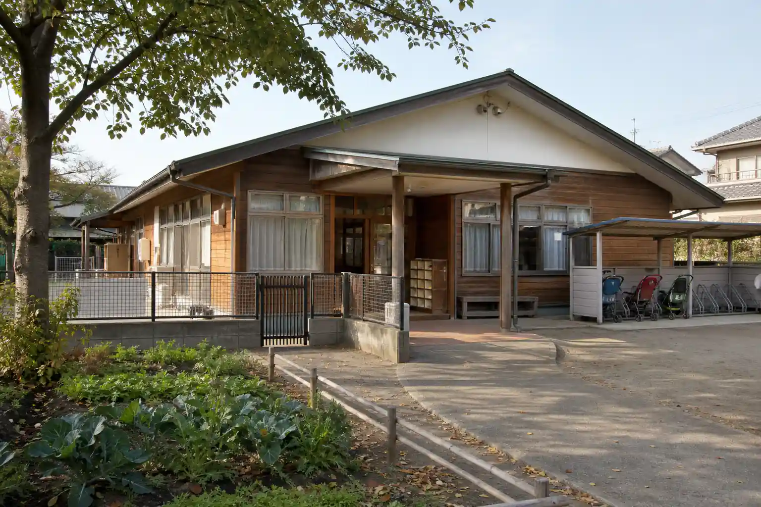 菜園と低い門、ベビーカー置き場のある平屋の保育園舎